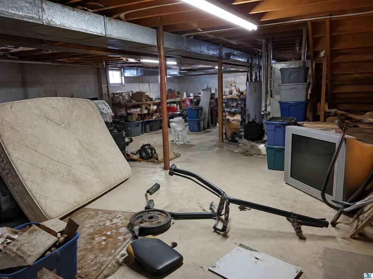 Basement filled with an old mattress, TV and debris before removal
